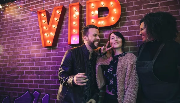 Group of friends standing in front of the VIP lighted sign, enjoying their Ultimate Inclusive ticket package at the World Famous Wax Museum, Madame Tussauds New York.