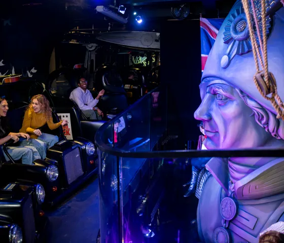 People sitting in taxi cabs on the Spirit of London ride at Madame Tussauds London, pointing at a recreation of Nelson's Column