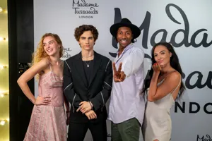 Three people standing with a figure of Timotheé Chalamet in an awards red carpet setting