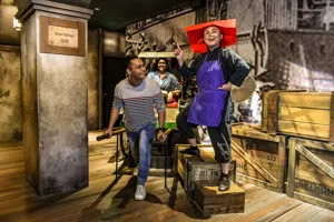 A set up of Singapore's history in the 1900s, depicting Keppel Harbour. A realistic wax figure of a Samsui woman beams as she stands on two boxes. A happy man holds the handles of the rickshaw and acts like he is pulling it with a girl seated behind.